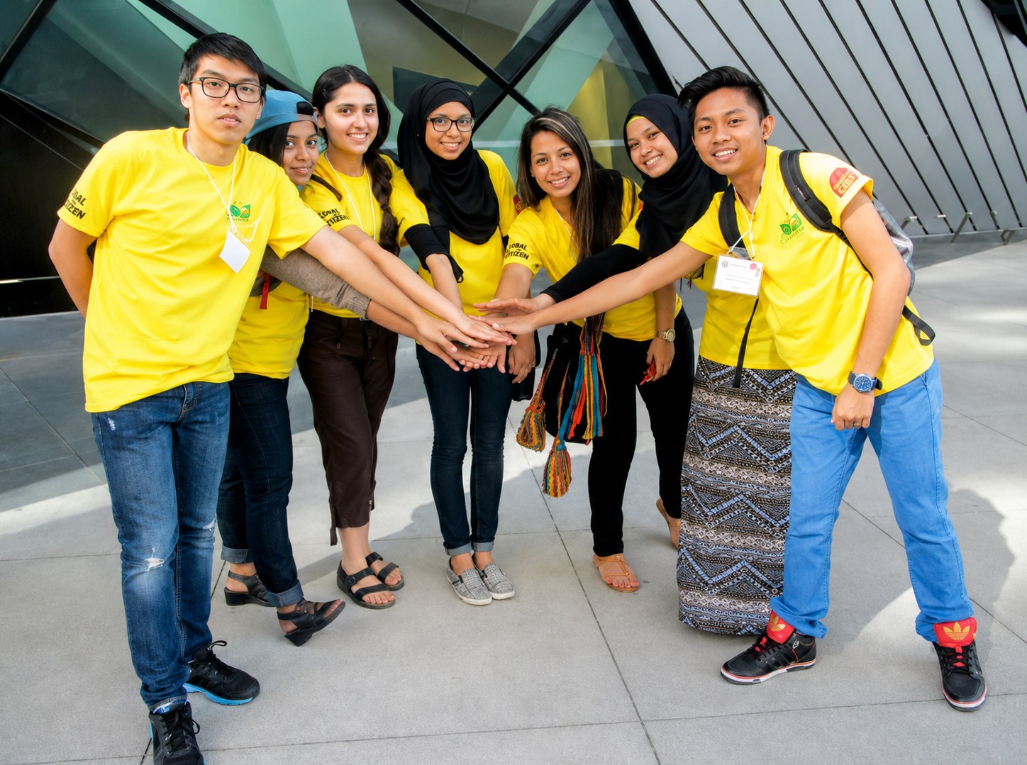 Group of newcomer youth in matching t-shirts joining hands together
